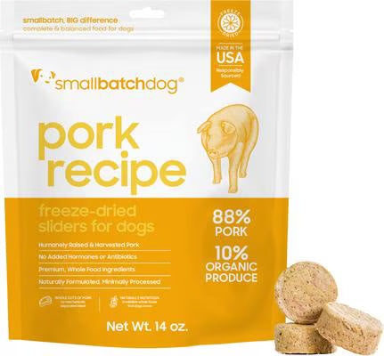 A stand-up pouch of Small Batch Dog 'Pork Recipe' freeze-dried sliders for dogs, shown on a white background with three dog sliders in the lower right corner. The packaging is white and orange, with a yellow-orange band across the bottom and a small pig illustration.